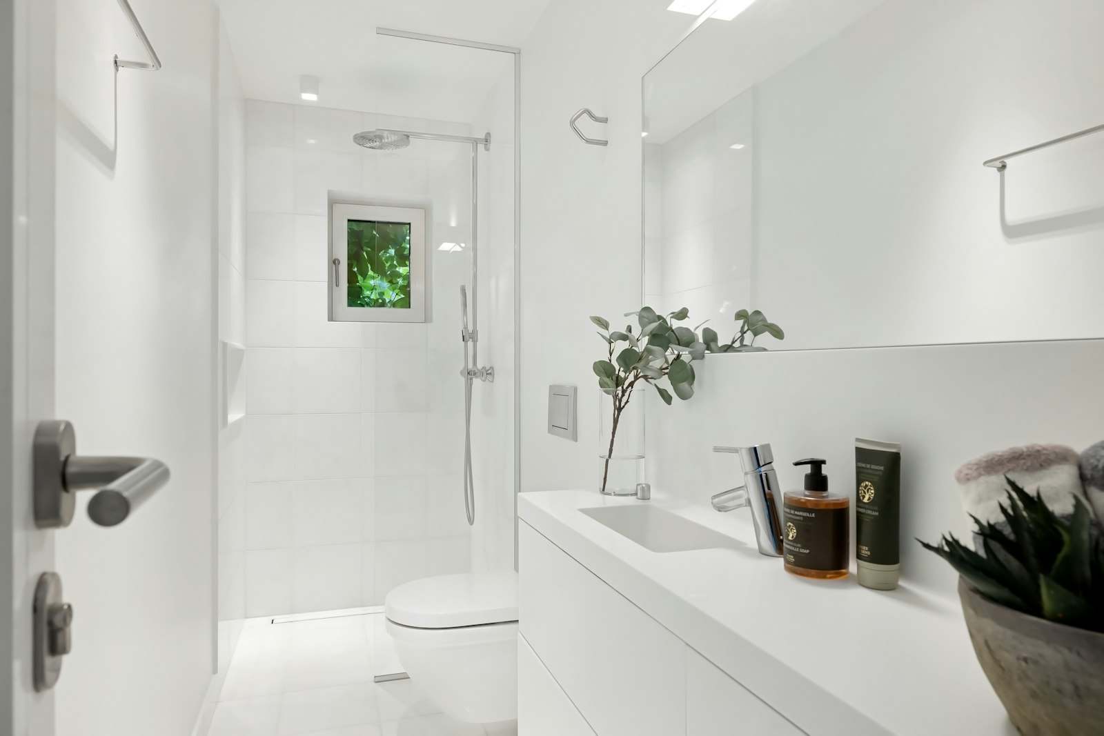 Baño blanco y luminoso con ducha a ras de suelo y mampara de cristal